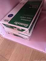 Two unopened packages of Grand & Toy foolscap premium copy paper stacked on shelf, each containing 500 sheets.