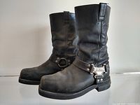 Full side profile of the boots showing mid-calf height, black leather material, and ankle harness with metal Harley Davidson badge.