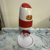 Front view of Jelly Belly electric ice crusher with ice chute and catch tray, showing Jelly Belly logo and red accents.