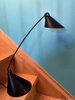 Photo showing the full lamp, illustrating the slender curved adjustable neck, conical base, and conical lampshade head in matte black.