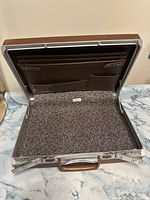 Open attache case showing interior compartments for documents and pens, grey patterned lining inside
