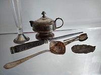Photo of the entire lot showing tall bud vase, small teapot, ladle, tongs, small spoon, all tarnished silverware