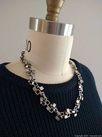 Necklace displayed on mannequin wearing dark blue knit top, showing full length and design of geometric cubist links in pewter metal.