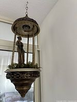 Full view of hanging lamp showing ornate metal top, chain, oil drip wires and goddess statue