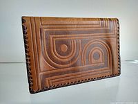 Front view of the vintage vegetable-tanned leather wallet showing the mid-century modern tooled geometric op-art pattern and braided leather trim around edges.