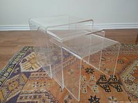Set of three clear lucite nesting waterfall tables arranged side by side showing different sizes.