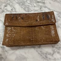 Photo of vintage genuine brown snakeskin clutch purse resting closed showing texture and shape.