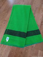 Folded green wool blanket with dark green stripe on hardwood floor