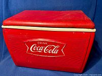 Front view of red metal Coca-Cola cooler showing rectangular shape and logo plate.