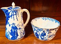 Front view of pitcher with lid and cranberry bowl side by side showing blue transferware design.