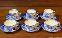 Two sets of three blue and white Royal Crown Derby Mikado pattern teacups and saucers arranged in two rows on a wood surface