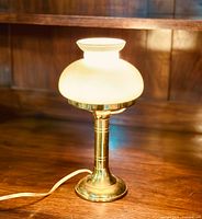 The full lamp illuminated on a wood surface, showing the brass base and stem with a glowing white glass shade.