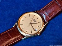 Close-up of the Seiko Quartz watch dial showing gold-tone face, black markings, and date window at 3 o'clock.