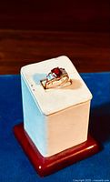 Front angle of the gold plated sterling silver ring featuring a large oval fire topaz center stone and clear cubic zirconia stones on either side, displayed on a white ring holder with a red base on a wooden surface.
