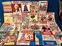 Wide view of the vintage MAD magazines collection arranged on a blue background. Shows 23 various issues and special editions spanning decades.
