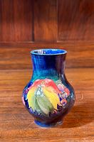 Frontal view of blue glazed vase with multicolour leaf and berry motif