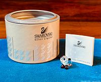 Mini panda bear figurine in front of original Swarovski silver crystal box and certificate booklet, with blue fabric background.