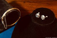 Gold-washed sterling silver bangle displayed on a black bracelet holder next to a pair of ornate Boyd Bond Sterling screw-back earrings on black display.