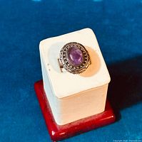 Front and top view of vintage sterling silver ring with oval purple amethyst stone set in decorative bezel with beading and swirling engraved silver.