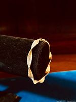 Front angled view of wide twist sterling silver bracelet showing woven texture and shiny gilt surface, displayed on black jewelry stand.