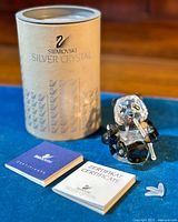 Swarovski Silver Crystal cylindrical box with certificate booklet and panda figurine on blue surface.
