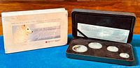 Outer cardboard sleeve and open black clamshell case with four coins