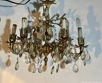 View of the chandelier showing five arms with candle-style light fixtures, some facetted glass droplets missing, brass with patina visible on arms and central structure.