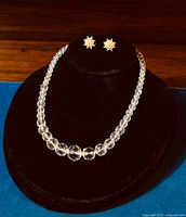 Clear graduated crystal bead necklace displayed on black bust with gold-tone starburst seed pearl-like clip earrings on top.