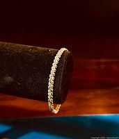 Fancy link sterling silver bangle bracelet displayed on black velvet stand with wooden background and blue surface.