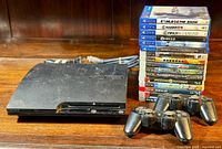 Overview of PS3 console, controllers, cables, and stacked game cases on wood surface