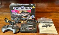 Front view showing the SEGA Genesis Mini console, one controller, power adapter, HDMI cable, original box and instruction manual.