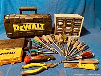 Overall lot display showing DeWalt angle grinder case, various hand tools including screwdrivers, chisels, pliers, a yellow case with bits, and a small parts organizer.