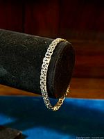 Bracelet displayed on a black cylindrical stand showing detailed woven V-style fancy silver link design.