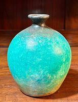 Front view of a turquoise Raku pottery spherical vase on a wooden surface.