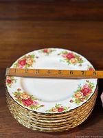 Stack of plates with a ruler showing approximately 8" diameter and gold trim