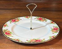 Front angled view of the Royal Albert Old Country Roses cake stand on a wooden surface, showing the floral patterned porcelain and silver metal handle.
