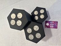 Top view of three black hexagonal coin trays each holding four silver Canadian quarters.