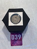 Silver half crown coin displayed in a protective holder on a black hexagonal box.