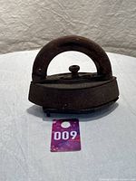 Photo of antique cast iron sad iron with thick wooden handle, showing front angle, placed on cloth with a tag 600 visible.