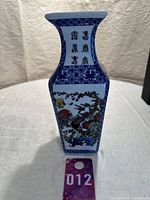 Porcelain vase with blue and white Asian design, floral and birds, showing front face with script and artwork, placed next to lot tag 012