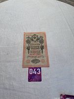 Photo showing the full view of the 1909 Russian 10 Ruble banknote lying flat on a surface with a purple lot number tag 043 below it.
