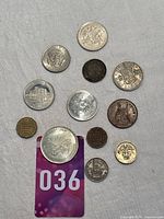 Lot of 12 varied metal coins and tokens laid out on grey fabric, showing different sizes, shapes and designs including heraldic and architectural motifs.