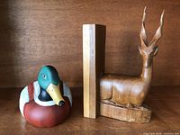 Pair of bookends: ceramic duck and wooden gazelle figurine side by side on wooden surface.