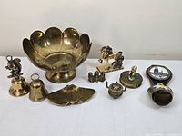 Photo showing assortment of brass and bronze items including lotus bowl, bells, unicorn figurine, candle holder and other small decorative pieces.