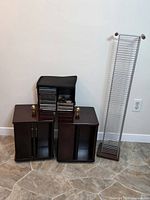 Photo of two Bombay brand CD holders and one metal CD tower against wall on tiled floor.