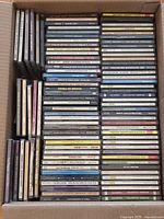 Top view of boxed lot showing stacked assorted music CD jewel cases with titles and spines visible for identification.