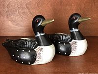 Photo showing pair of matching ceramic loon coin banks, black and white with red eyes and greenish beaks, sitting side by side.