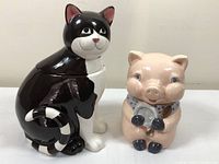 Two ceramic cookie jars: a black and white cat and a pink pig, shown side by side on a white surface.