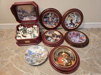 Photo showing six decorative plates and one red wooden Christmas-themed music box with snowy village scene inside.
