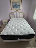 Full view of assembled double bed with brass headboard, mattress, and box spring in room corner.